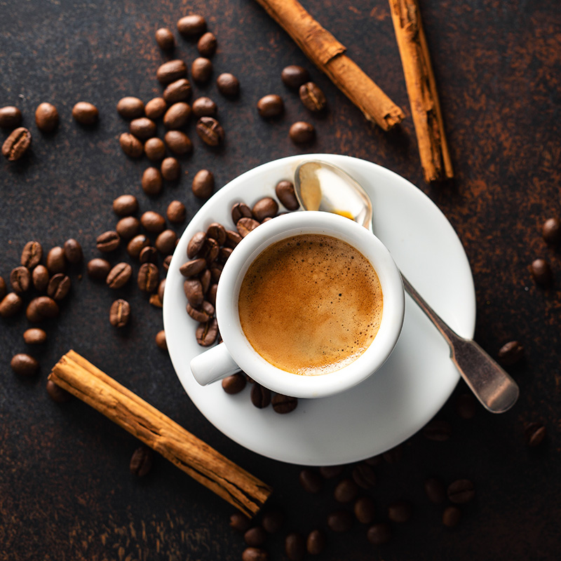 Gros plan sur une tasse de café entourée de grains de café, illustrant la qualité et l'arôme riche de nos solutions café professionnelles.